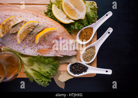 Trota fresca e ingredienti per preparare piatti a base di pesce sulla tavola nera Foto Stock