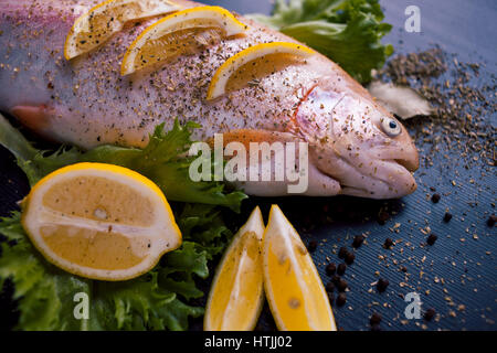 Trota fresca e ingredienti per preparare piatti a base di pesce sulla tavola nera Foto Stock