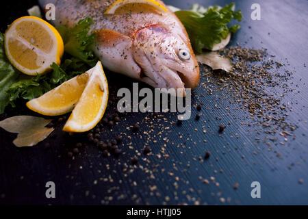 Trota fresca e ingredienti per preparare piatti a base di pesce sulla tavola nera Foto Stock