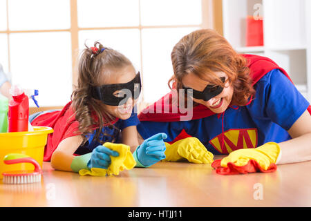 Carino donna e di sua figlia di capretto vestiti come supereroi la pulizia del pavimento e sorridente Foto Stock