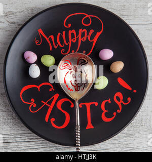 Felice Pasqua scritte a mano il preventivo scritto su piastra nera con il coniglietto di pasqua disegno su vintage cucchiaio d'argento. Immagine quadrata Foto Stock