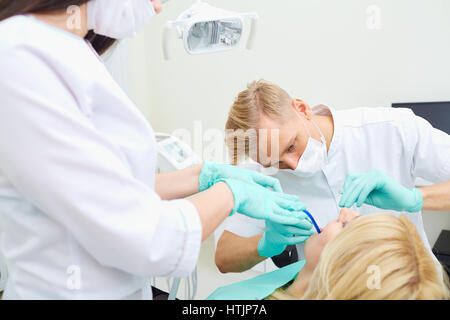 Il dentista uomo e donna assistente sono il trattamento di denti per client in studio dentistico. Foto Stock