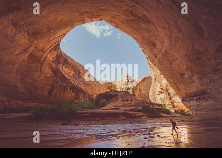 Ampio angolo di visione dei maschi di escursionista backpacking sotto splendide Jacob Hamblin Arch in Coyote Gulch in una giornata di sole con cielo blu e nuvole in estate, Utah Foto Stock
