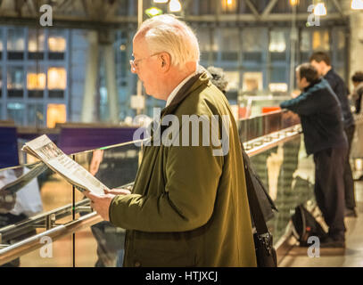 Un uomo anziano legge un giornale in attesa di un treno Foto Stock