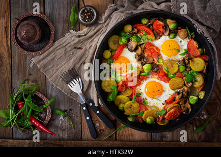 La prima colazione per due persone. Uova fritte con verdure - shakshuka in una padella su un sfondo di legno in stile rustico. Lay piatto. Vista superiore Foto Stock
