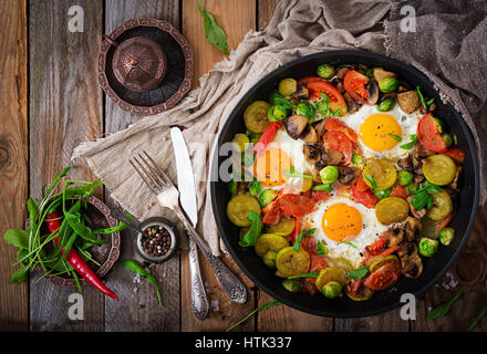 La prima colazione per due persone. Uova fritte con verdure - shakshuka in una padella su un sfondo di legno in stile rustico. Lay piatto. Vista superiore Foto Stock