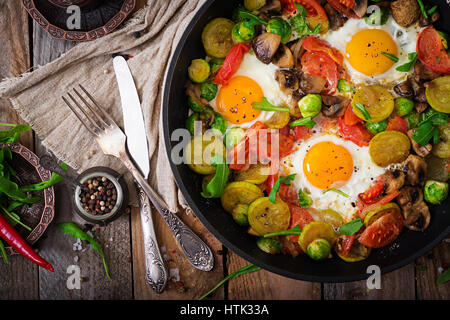 La prima colazione per due persone. Uova fritte con verdure - shakshuka in una padella su un sfondo di legno in stile rustico. Lay piatto. Vista superiore Foto Stock