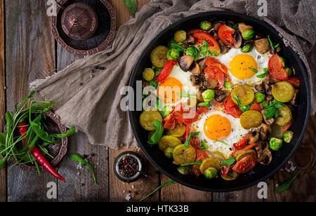 La prima colazione per due persone. Uova fritte con verdure - shakshuka in una padella su un sfondo di legno in stile rustico. Lay piatto. Vista superiore Foto Stock