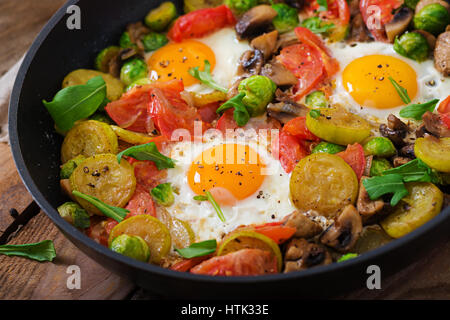 La prima colazione per due persone. Uova fritte con verdure - shakshuka in una padella su un sfondo di legno in stile rustico. Foto Stock