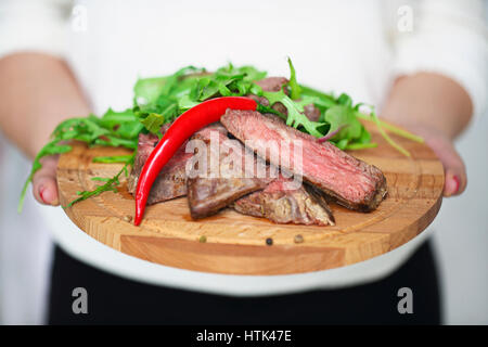 Fette di mezzo raro grigliate di carne di manzo bistecca con insalata di rucola nelle mani di una donna Foto Stock