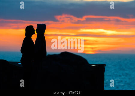 Aberystwyth Wales UK, domenica 12 marzo 2017 UK Meteo: una giovane coppia e abbraccio bacio come dietro di loro il sole tramonta spettacolarmente su acque di Cardigan Bay off Aberystwyth sulla West Wales coast. Photo credit Credito: keith morris/Alamy Live News Foto Stock