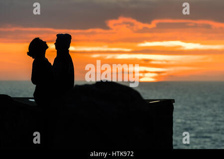 Aberystwyth Wales UK, domenica 12 marzo 2017 UK Meteo: una giovane coppia e abbraccio bacio come dietro di loro il sole tramonta spettacolarmente su acque di Cardigan Bay off Aberystwyth sulla West Wales coast. Photo credit Credito: keith morris/Alamy Live News Foto Stock