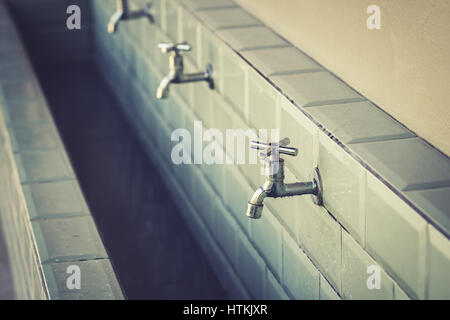 Fila di rubinetti di acciaio in una grande stanza da bagno Foto Stock