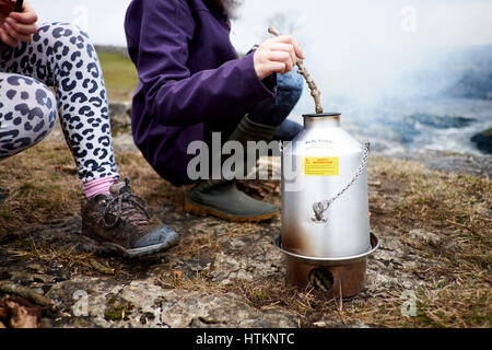 Due bambini all'aperto intorno a un Kelly bollitore stufa a legna bollitore alimentando in legno Foto Stock