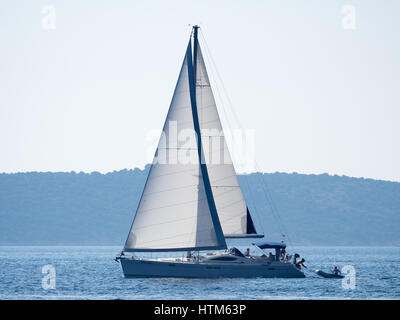 Una barca a vela barca a vela bianche vele vela sul mare Mediterraneo sotto un cielo blu sulle calme acque al largo della costa della Croazia Foto Stock