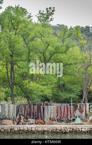 Colorate reti da pesca e galleggia memorizzati appeso su una pietra costruito quay da acqua calma sotto un gruppo di lussureggianti alberi di alto fusto, Porto di Sipan Croazia Foto Stock