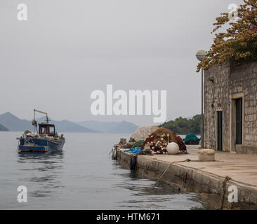 Barca da pesca lasciando quay quayside con reti da pesca e di boe all'alba, in acque tranquille, con lo sfondo delle isole, Croazia Foto Stock