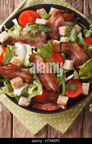 Insalata di pancetta fritta, pomodoro, crostini e lattuga close-up su una piastra su un tavolo. Vista verticale da sopra Foto Stock