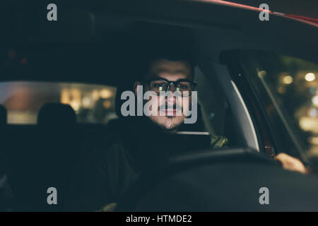 Giovane uomo bello utilizza lo smartphone nella sua auto di notte - pericoloso, tecnologia, il concetto di driver Foto Stock