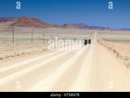 Due motorini guida veloce sul lungo rettilineo di strada nel deserto. Foto Stock