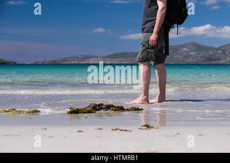 Giovane maschio caucasico facendo una passeggiata su una spiaggia di sabbia bianca con acque turchesi sulla sua vacanza Foto Stock