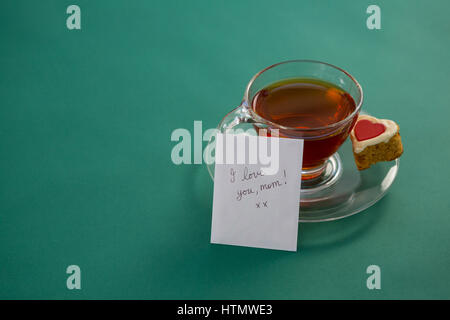 Tè con forma di cuore cookie e ti amo mamma testo sulla scheda contro lo sfondo di colore verde Foto Stock