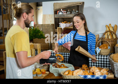 Un personale sorridente imballaggio pane pretzel nel sacchetto di carta al contatore nel panificio Foto Stock