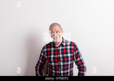 Senior Uomo in camicia controllati sorridente, studio shot contro bianco Foto Stock