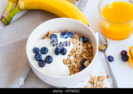 Muesli con yogurt e mirtilli, bananans e vetro di succo d'arancia e sana colazione pasto Foto Stock