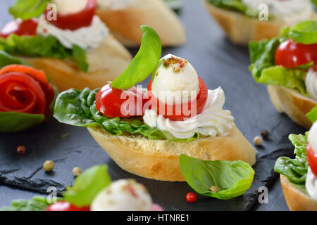 Deliziosi antipasti freddi: fette di baguette con cherry pomodoro, mozzarella, crema di formaggio, olio di oliva e le foglie di basilico Foto Stock