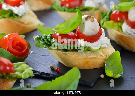 Deliziosi antipasti freddi: fette di baguette con cherry pomodoro, mozzarella, crema di formaggio, olio di oliva e le foglie di basilico Foto Stock