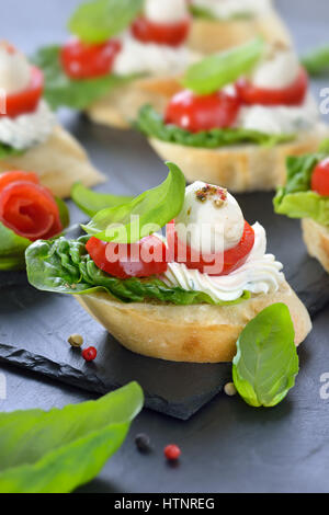 Deliziosi antipasti freddi: fette di baguette con cherry pomodoro, mozzarella, crema di formaggio, olio di oliva e le foglie di basilico Foto Stock