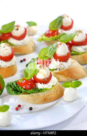 Deliziosi antipasti freddi: fette di baguette con cherry pomodoro, mozzarella, crema di formaggio, olio di oliva e le foglie di basilico Foto Stock