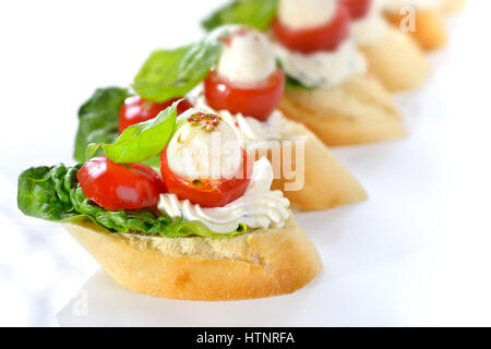Deliziosi antipasti freddi: fette di baguette con cherry pomodoro, mozzarella, crema di formaggio, olio di oliva e le foglie di basilico Foto Stock