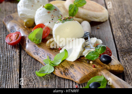 Italian mozzarella snack con pomodori ciliegia, basilico e olive servita su una tavola di legno con pane tostato Foto Stock