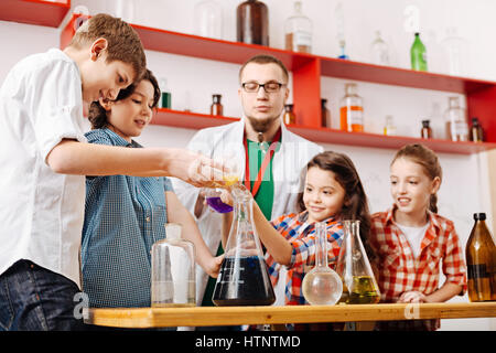 Il lavoro di squadra. Positivo felice felici i bambini in piedi intorno al tavolo e di effettuare un esperimento chimico mentre è entusiasta della scienza Foto Stock