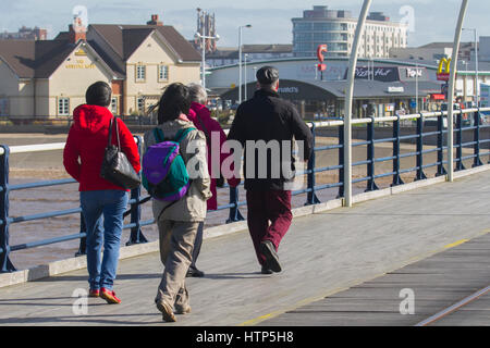 Southport, Merseyside, Regno Unito. Regno Unito Meteo. Il 14 marzo 2017. Luminosa e ariosa con un cielo azzurro per pier passeggini. Barmy marzo temperature continuare nel nord ovest, ma con un po' di più vento rispetto a quella di fine. Le persone sono ben confezionate fino contro la brezza del mare come essi passeggiata verso la fine del 2° molo più lungo in Inghilterra. Credito: MediaWorldImages/Alamy Live News Foto Stock