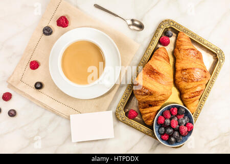 Una foto aerea di una tazza di caffè con lamponi freschi, mirtilli e croissant, con un fustellato business card con un posto per il testo Foto Stock