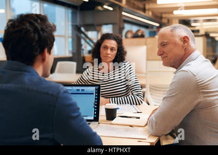 Gruppo diversificato di casualmente vestito colleghi professionisti parlare insieme di business pur avendo un incontro a una scrivania in un ufficio moderno Foto Stock