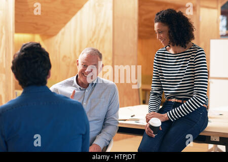 Gruppo diversificato di casualmente vestito colleghi professionisti sorridente e parlare insieme di business pur avendo un incontro a una scrivania in un ufficio moderno Foto Stock