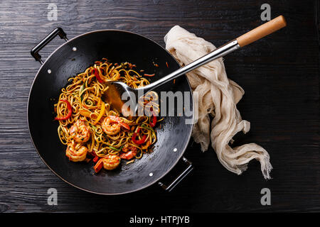 Udon stir fry tagliatelle con gamberi e gamberetti verdure in padella wok su nero bruciato sullo sfondo di legno Foto Stock