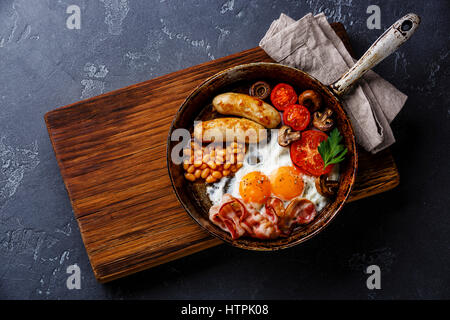 Prima colazione inglese nel recipiente di cottura con uova fritte, salsicce, bacon e fagioli in pietra scura sullo sfondo Foto Stock