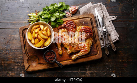 Grigliata di fritto di pollo arrosto Tabaka e Spicchi di patate sul bordo di taglio su sfondo di legno Foto Stock