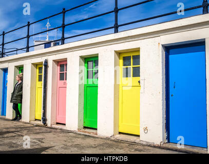 In una giornata di sole, una giovane donna si erge ad ammirare una fila colorata di porte color pastello nel porto di North Berwick Foto Stock