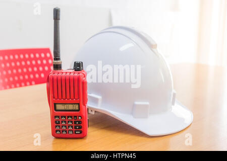 Red walkie-talkie radio e un bianco casco di sicurezza su sfondo di legno Foto Stock