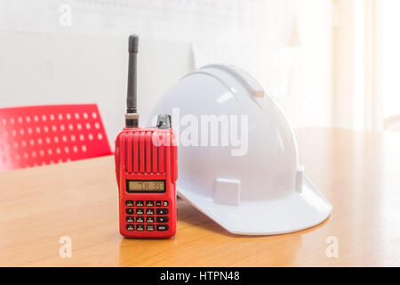 Red walkie-talkie radio e un bianco casco di sicurezza su sfondo di legno Foto Stock