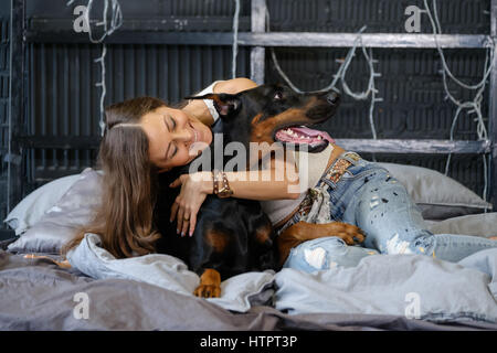 Giovane donna graziosa con nero cane doberman nel letto Foto Stock