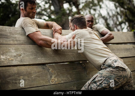 Soldati aiutare l uomo a salire la parete in legno in boot camp Foto Stock