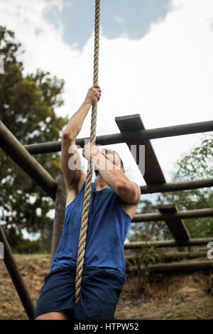 Montare l'uomo salendo una fune durante il percorso ad ostacoli in boot camp Foto Stock