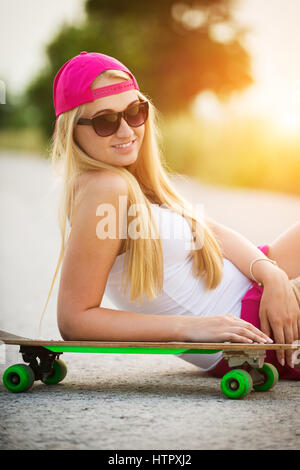 Attraente tanga sorridente ragazza adolescente con lo skateboard, immagine con la sunflare Foto Stock